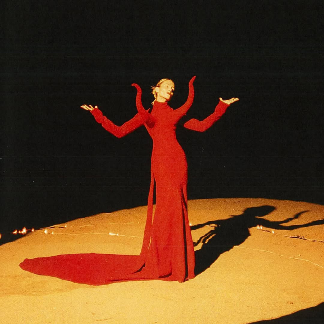 Older man wearing dark sunglasses and a navy sweater sitting at a table, holding a white gift box with a red ribbon, with text saying 'Sunnies that say "I know what I like"'.