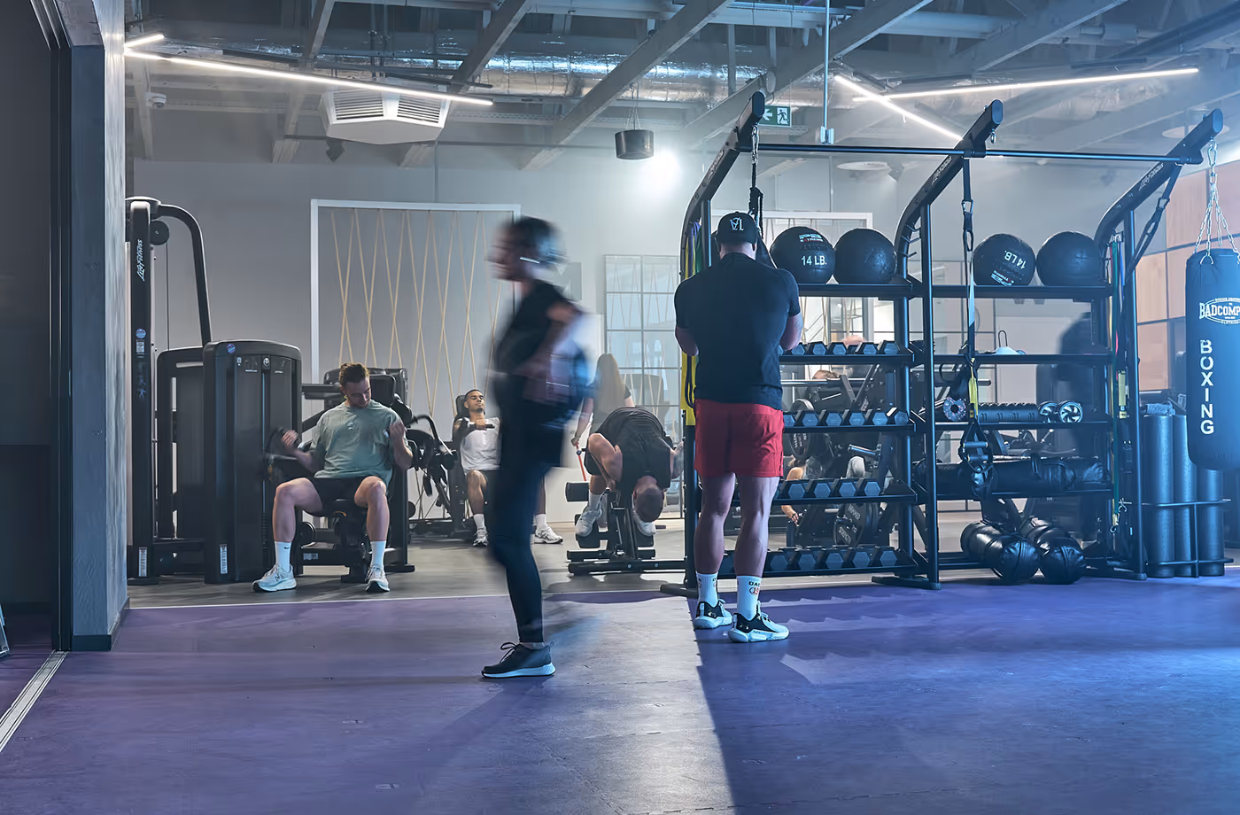 People exercising in a gym with weight machines, kettle bells, and a boxing bag.