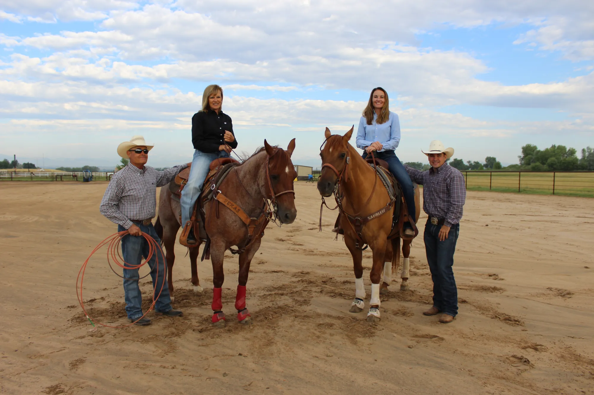 The Ellerman family with two horses in an outdoor arena, two riders mounted and two standing alongside