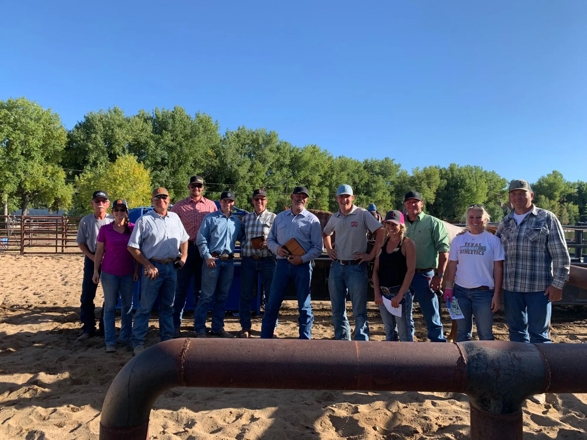 A group of roping school participants and instructors smiling together in a sunny arena