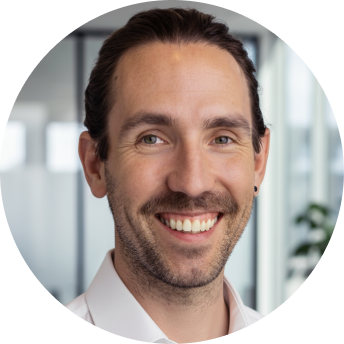 Smiling man with dark hair and a white shirt in a bright office setting.