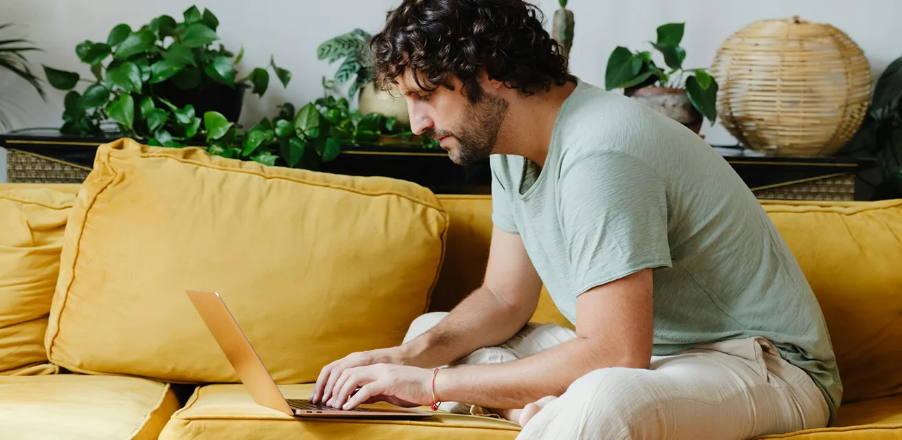 a man on a yellow sofa checking business statistics on a laptop