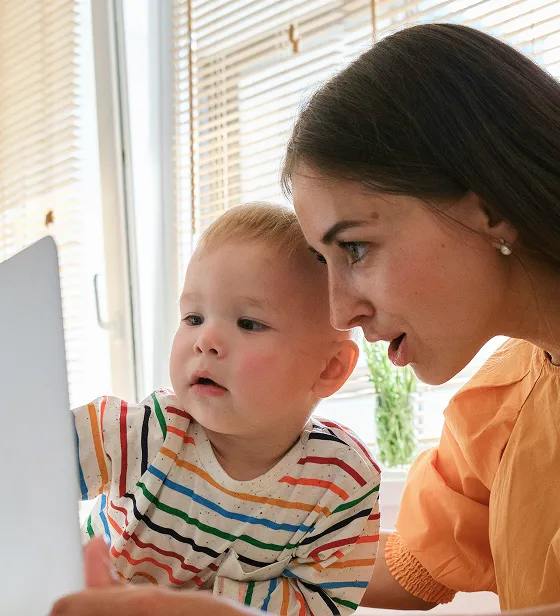a mom and young toddler looking at a computer screen