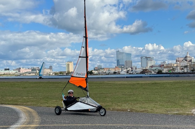 Land sailboat on pavement with city skyline and cloudy blue sky background