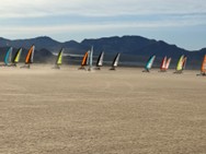 Colorful land sailboats race across flat desert landscape with mountains behind