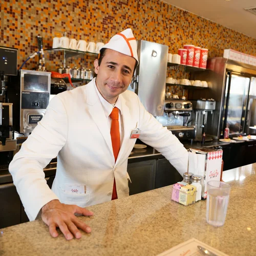 DailyPay Diner actor-server wearing the custom cap behind the counter