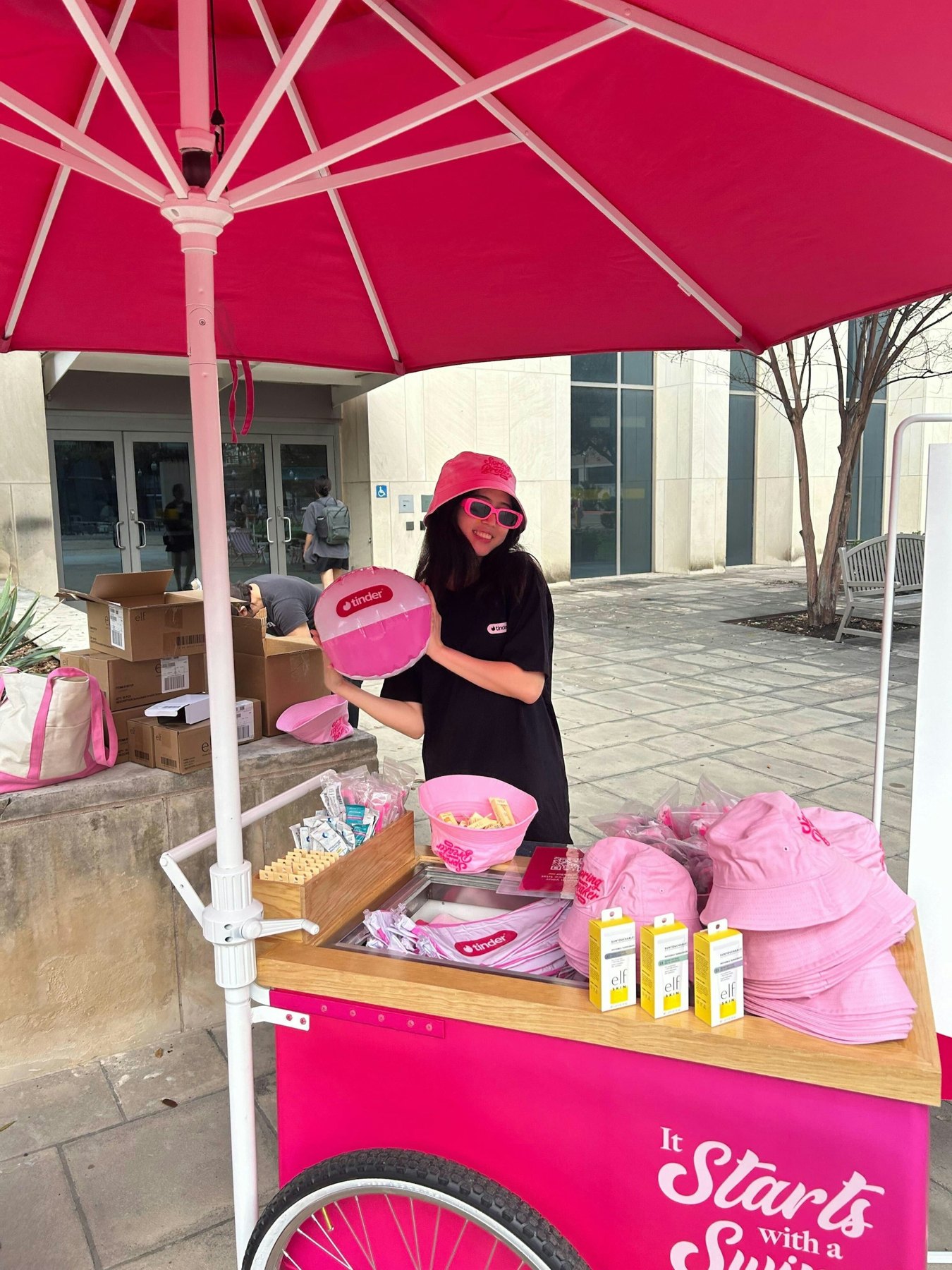 Tinder campus giveaway cart with pink bucket hats and cream-and-pink tote bags