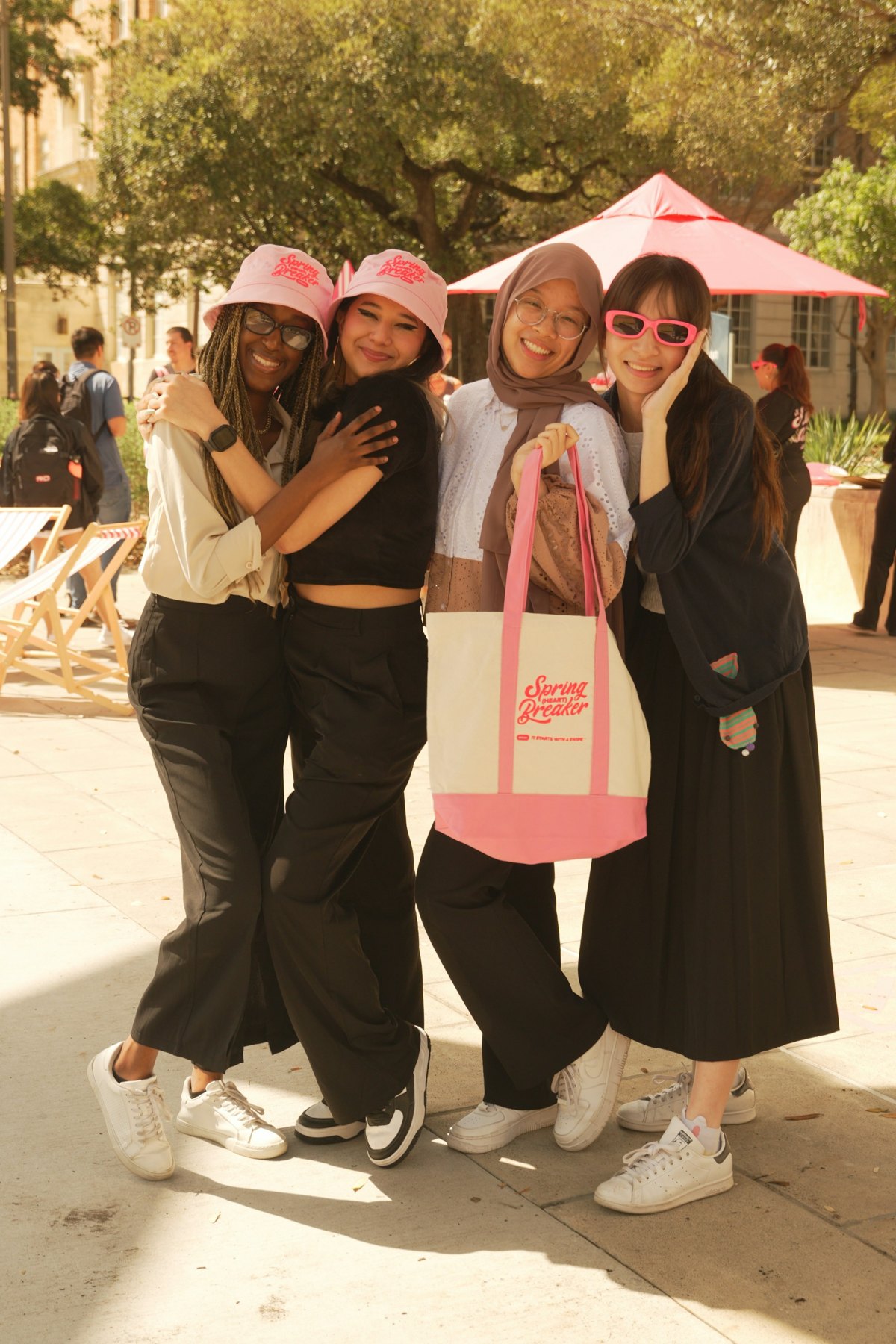 Students wearing pink Spring Heart Breaker bucket hats and carrying cream-and-pink Tinder tote bags