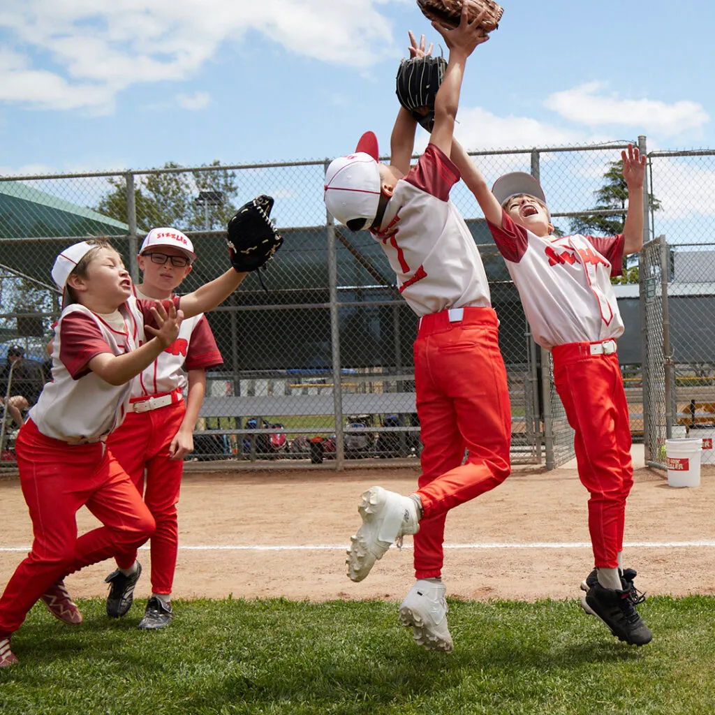 Young baseball players reaching for a ball in Sizzler cream and burgundy jerseys