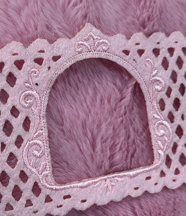 Close-up of the arched koozie opening, embroidered scrollwork and laser-cut felt on pink fur
