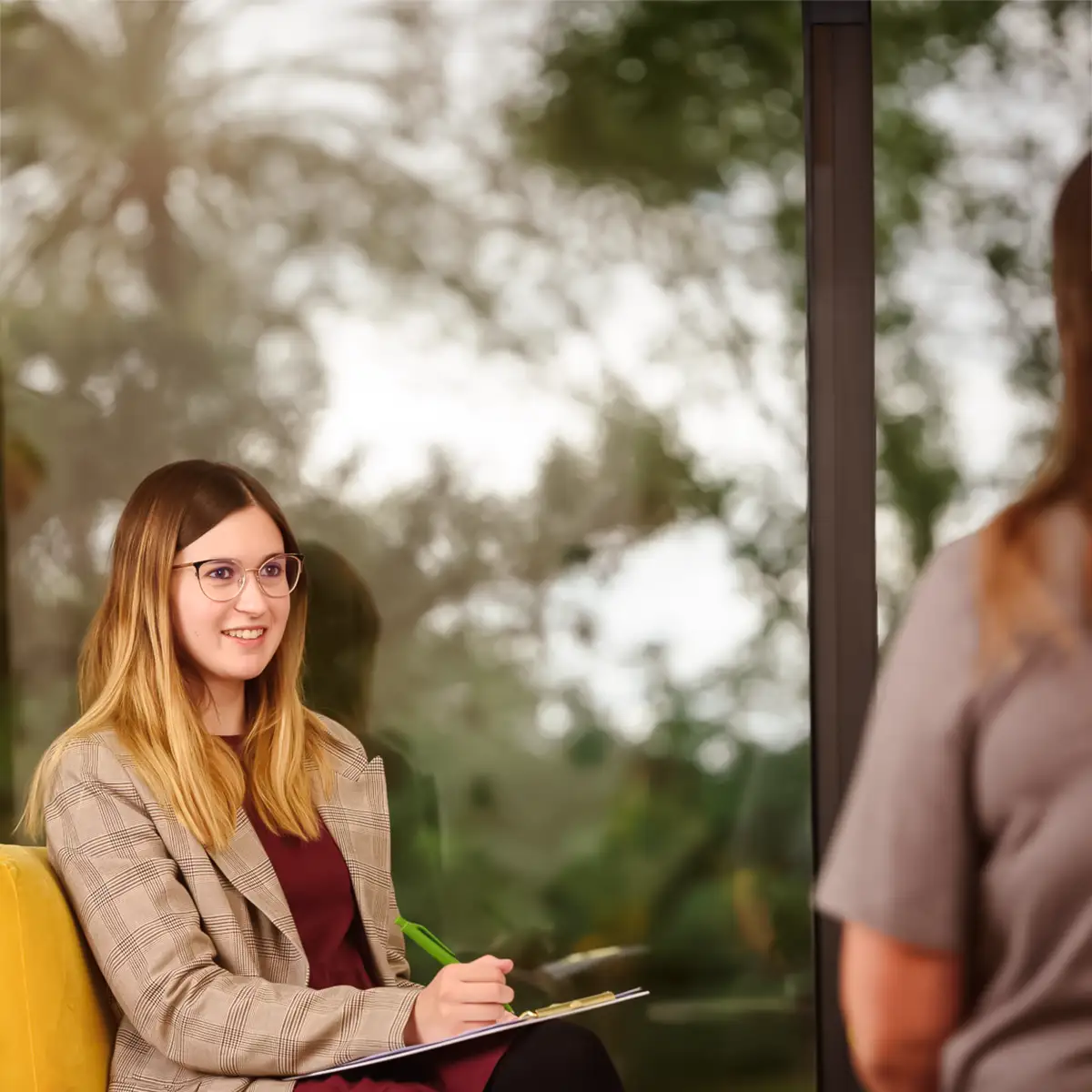 Therapeutin mit Klemmbrett auf dem Schoß im Gespräch mit einer Patientin 