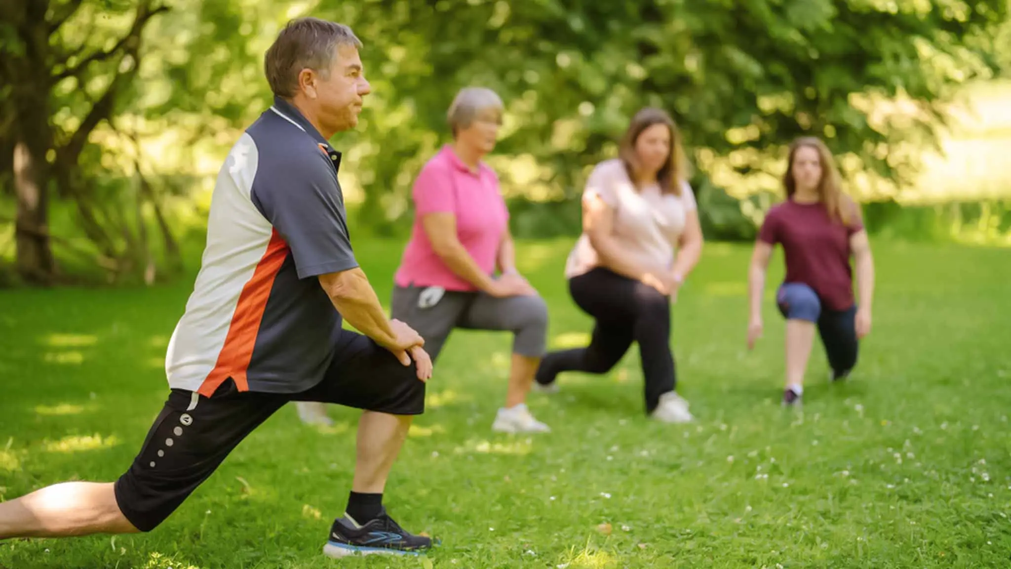 Drei Frauen und ein Mann dehnen sich gemeinsam auf einer Wiese.