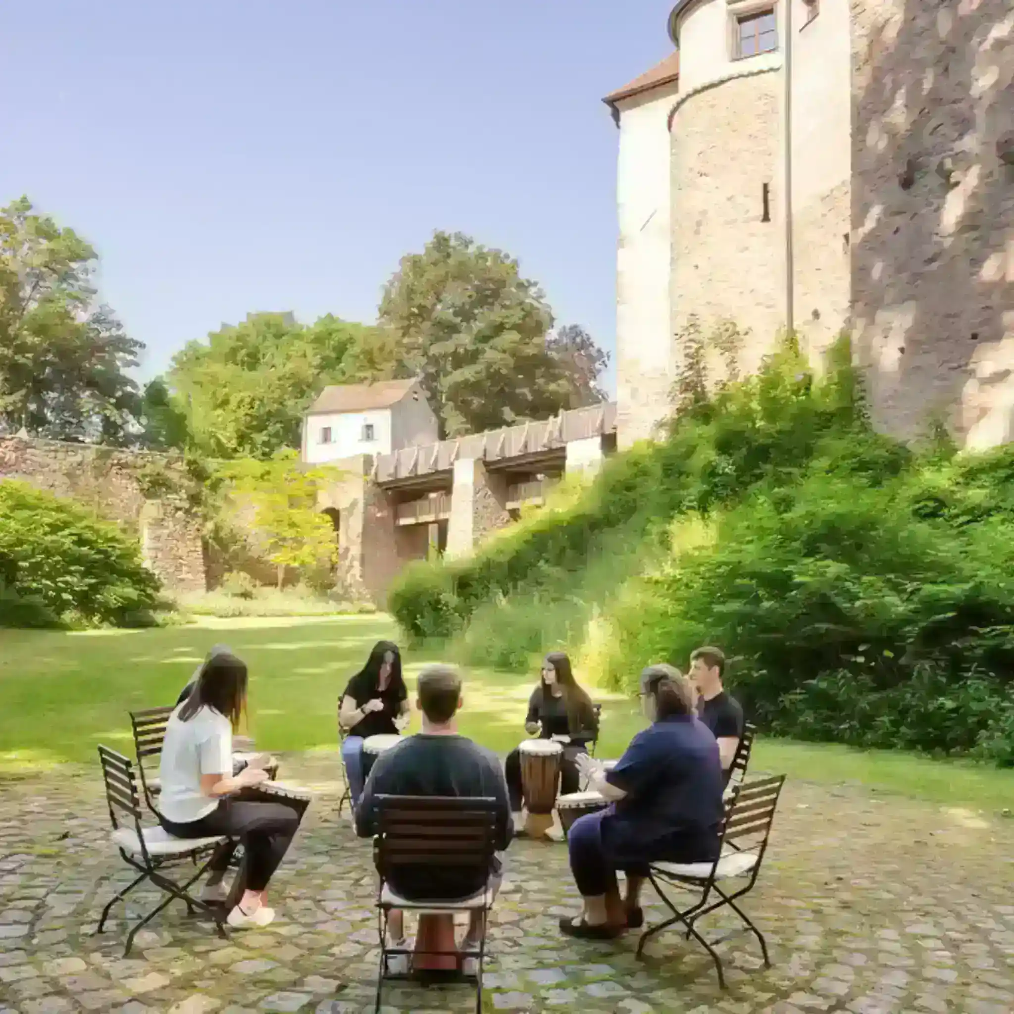 Mehrere Patienten sitzen draußen vor der Burg Wernberg in einem Stuhlkreis und spielen gemeinsam Musik.