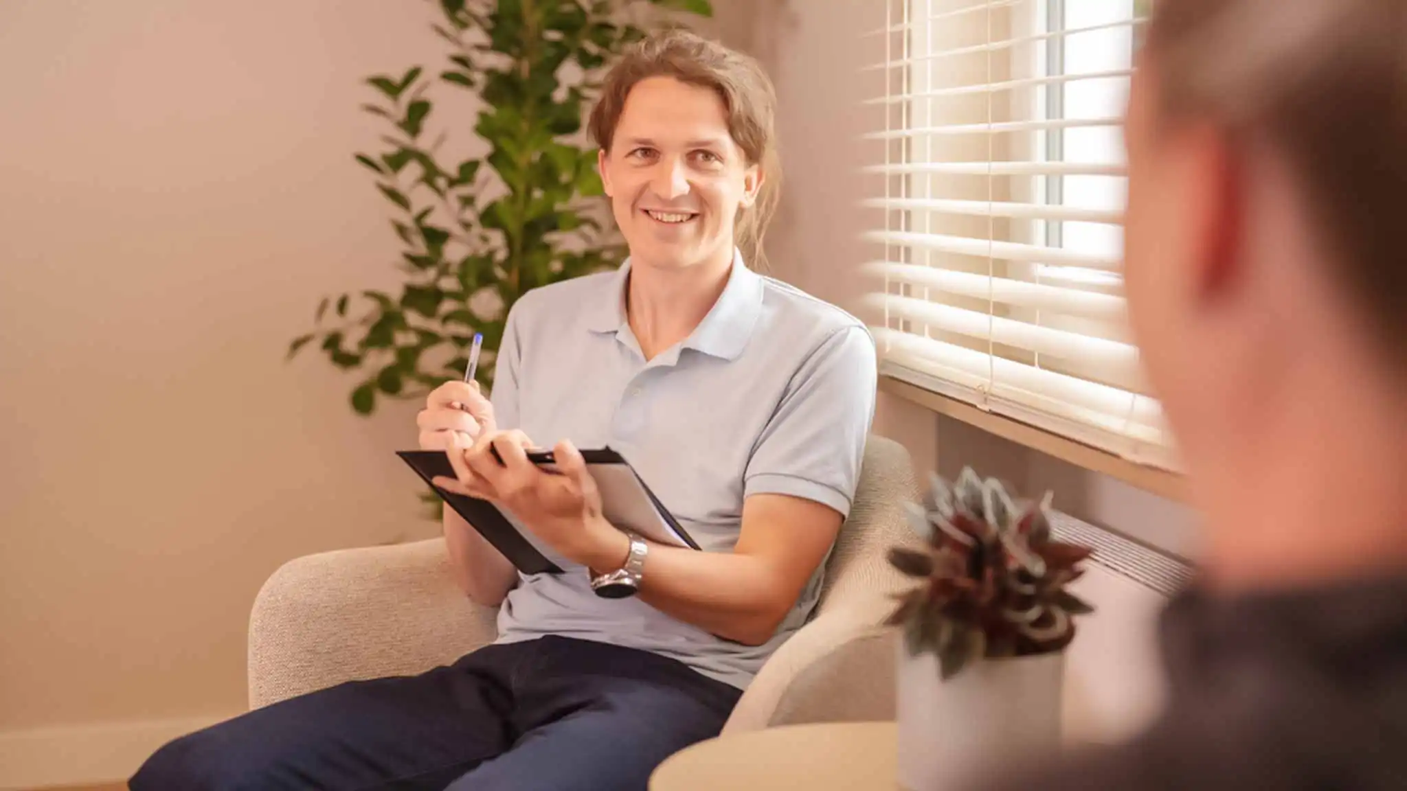 Ein Psychotherapeut hält seine Notizen in der Hand und spricht mit einem Patienten.