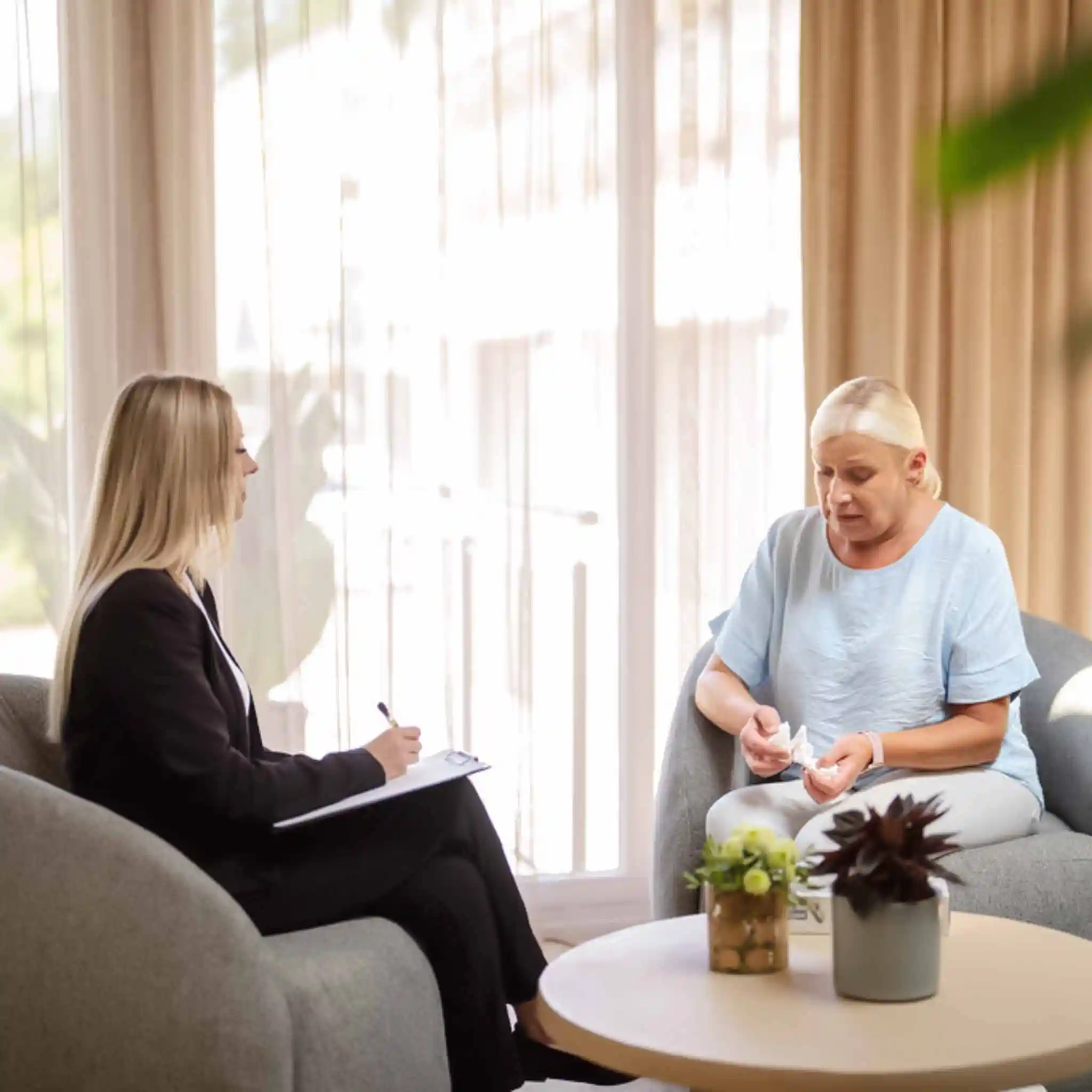 Eine Patientin und eine Psychotherapeutin sitzen sich in einem Therapiesetting gegenüber.