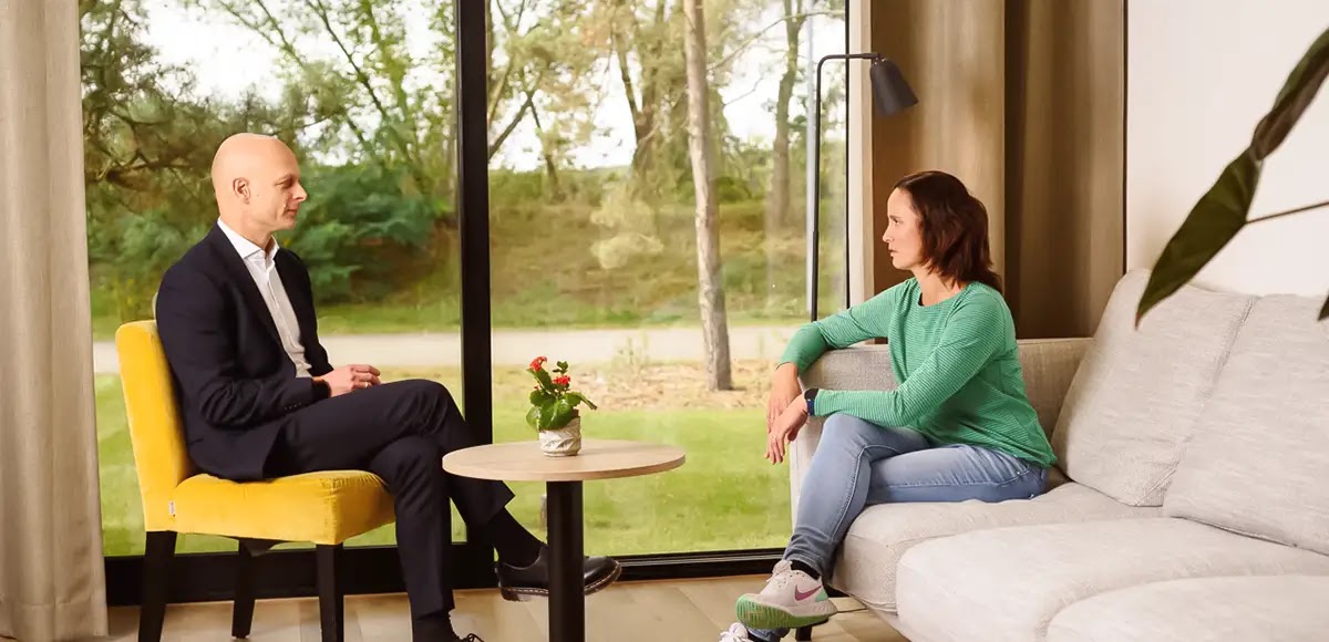 Eine Patientin sitzt auf einem Sofa, ihr gegenüber sitzt ihr Therapeut. Zu sehen sind beide in einer Seitenansicht.