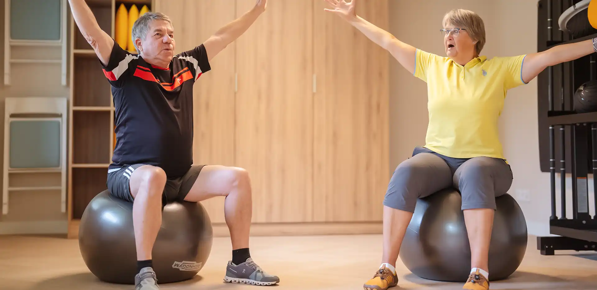 Ein Mann und eine Frau sitzen nebeneinander auf zwei Gymnastikbällen mit zur Seite gestreckten Armen.