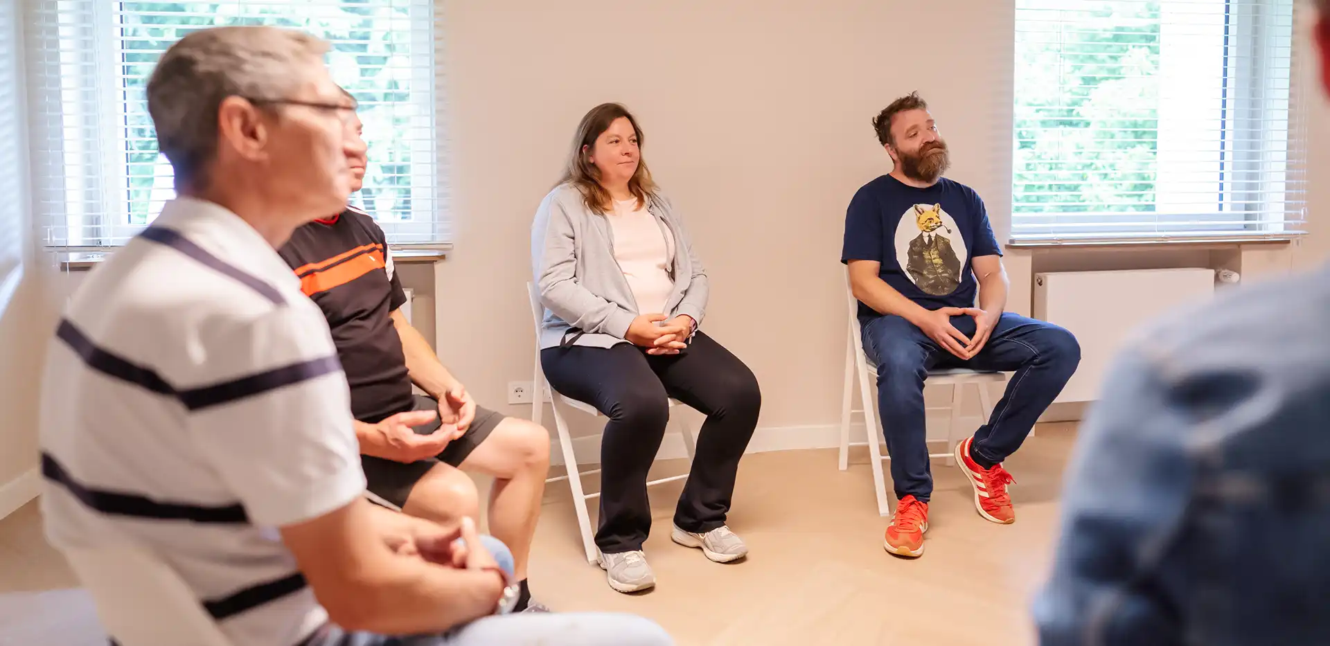 Mehrere Patienten sitzen bei einer Gruppentherapie im Kreis und hören gespannt zu.