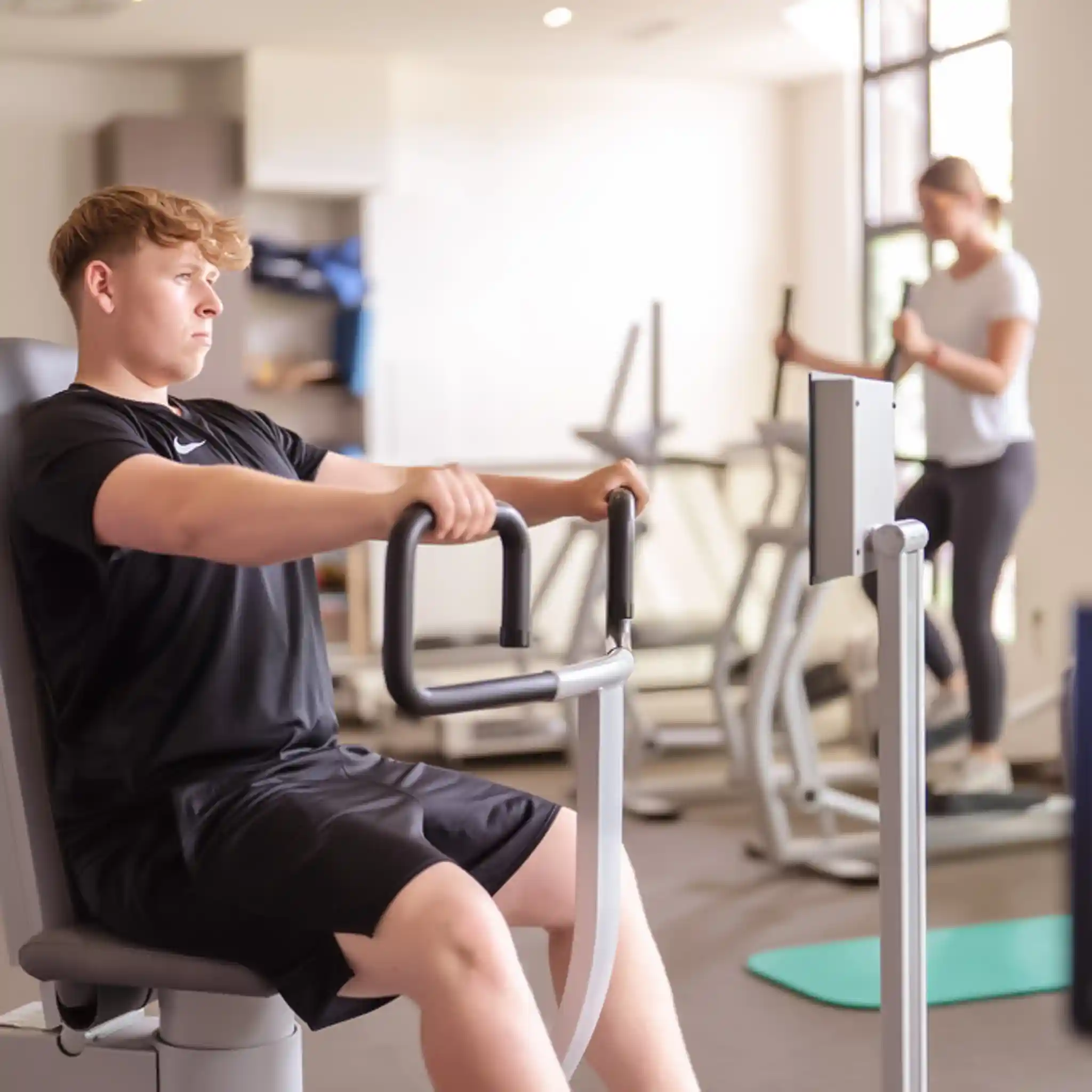 Ein Patient und eine Patientin trainieren an Geräten im Fitnessraum.