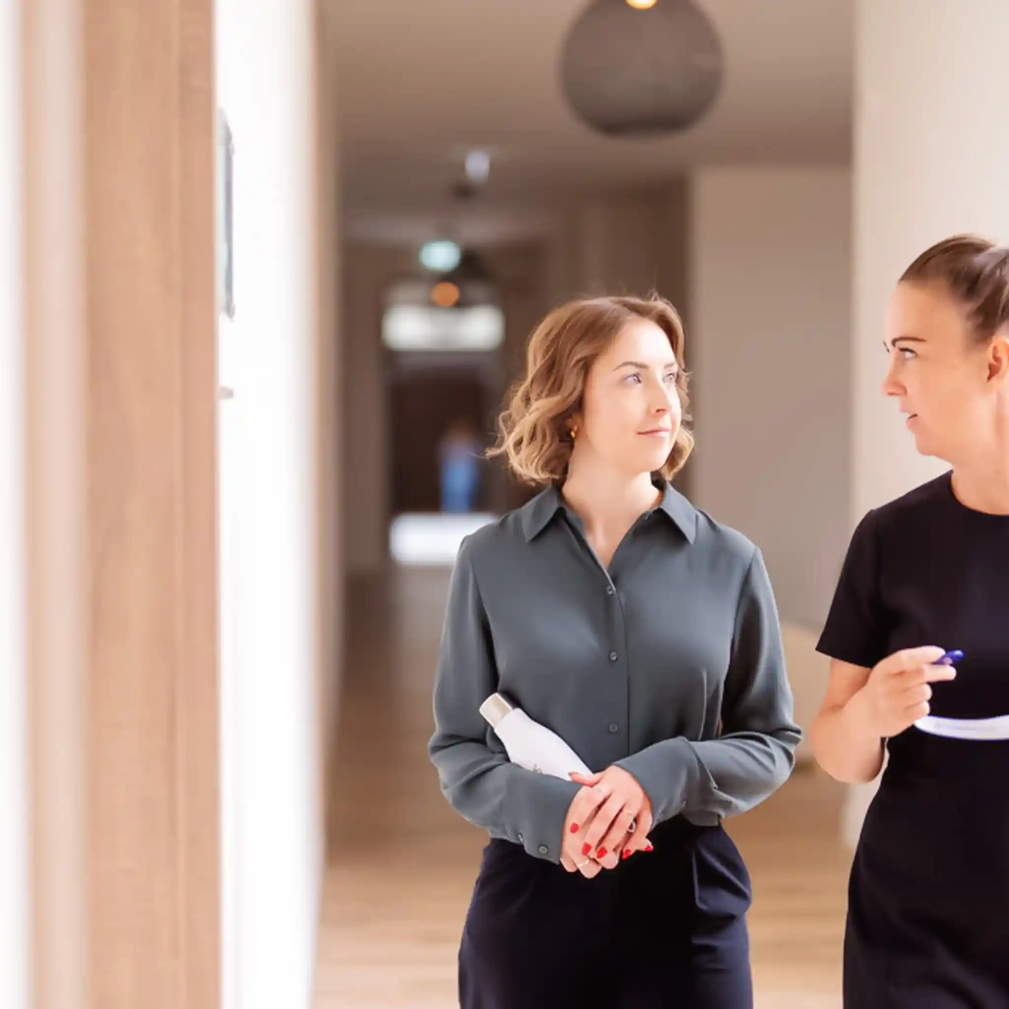 Eine Patientin und eine Therapeutin laufen zusammen den Gang entlang und unterhalten sich.