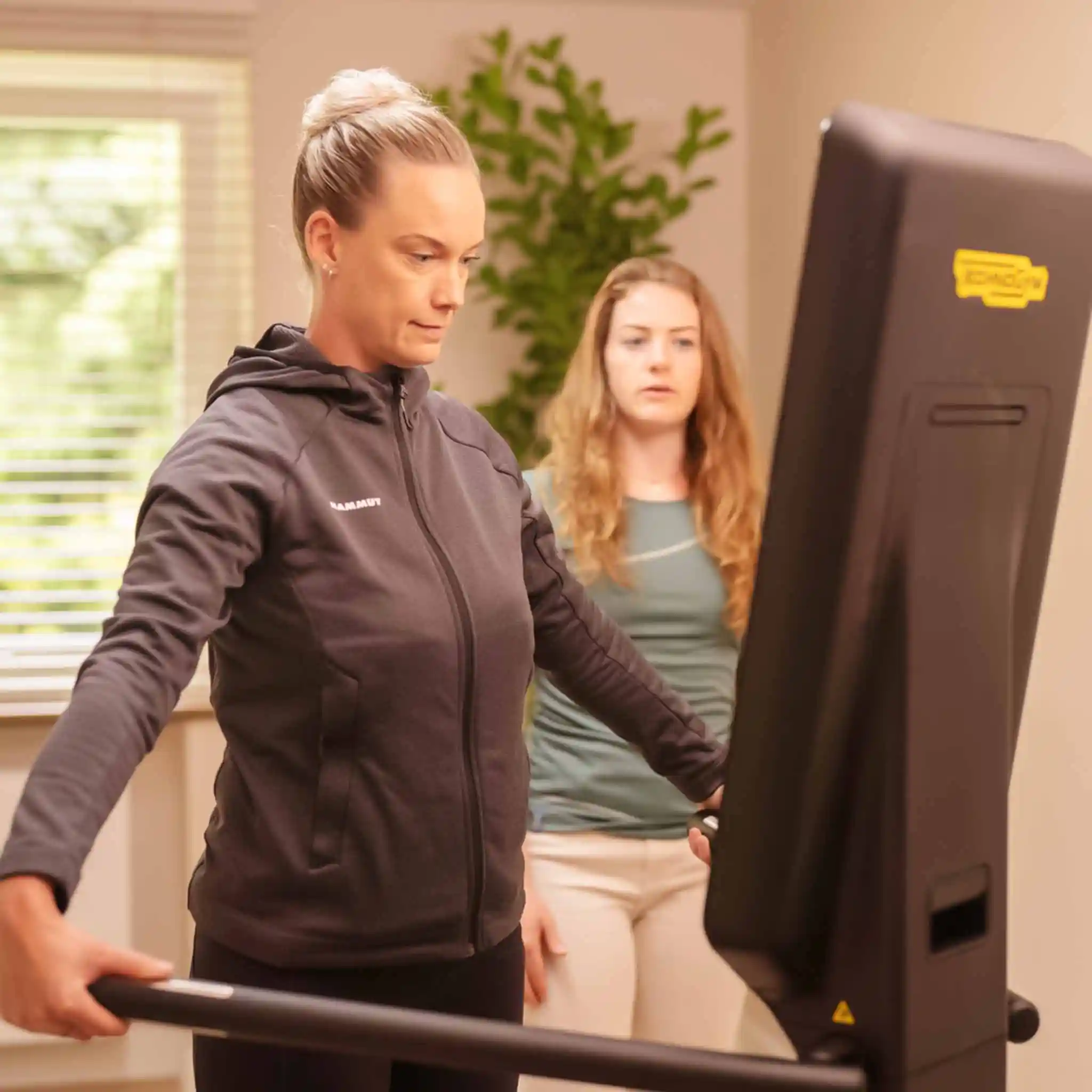 Eine Patientin trainiert auf einem Laufband. Neben ihr steht eine Therapeutin.