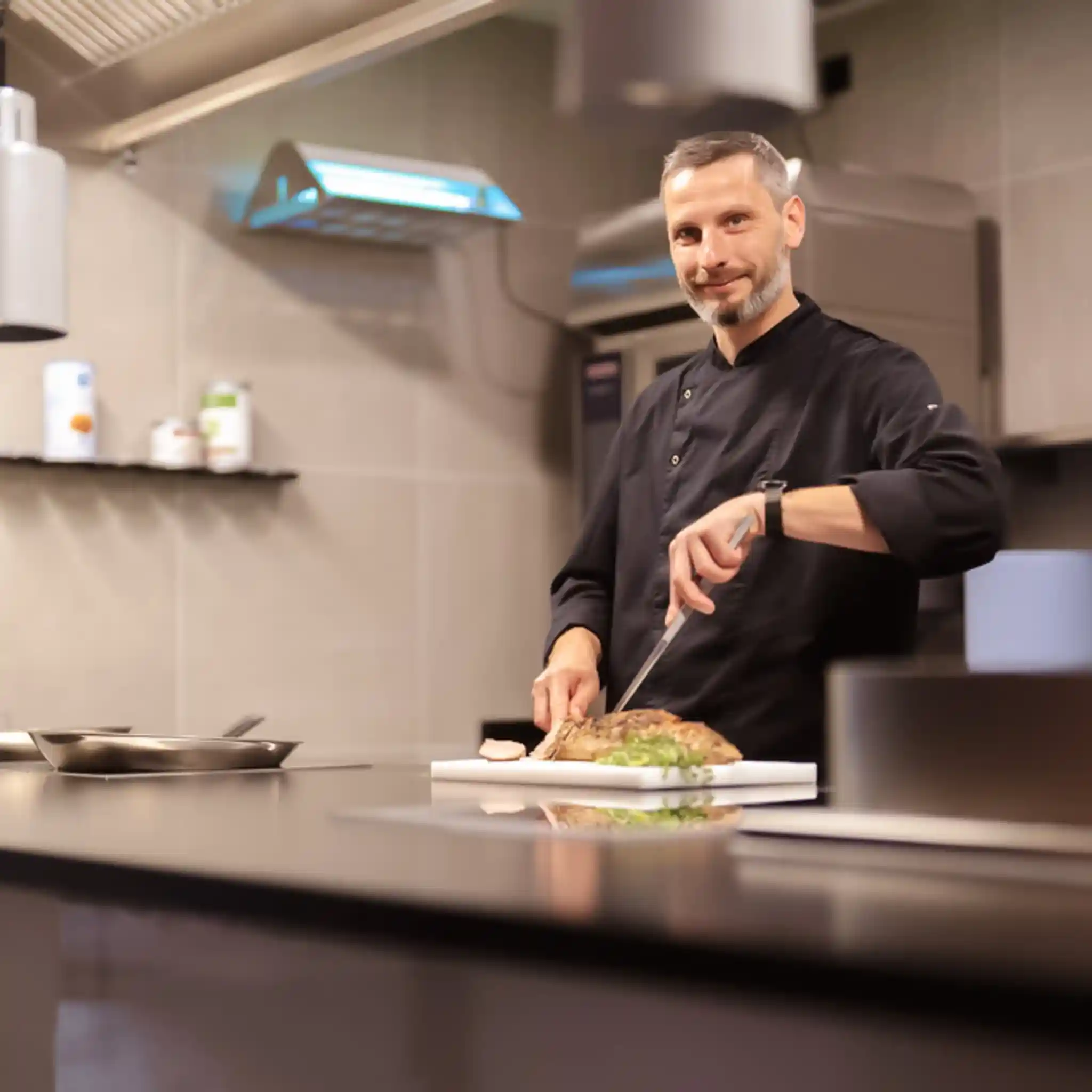 Eon Koch schneidet ein Stück Fleisch und lächelt in die Kamera.