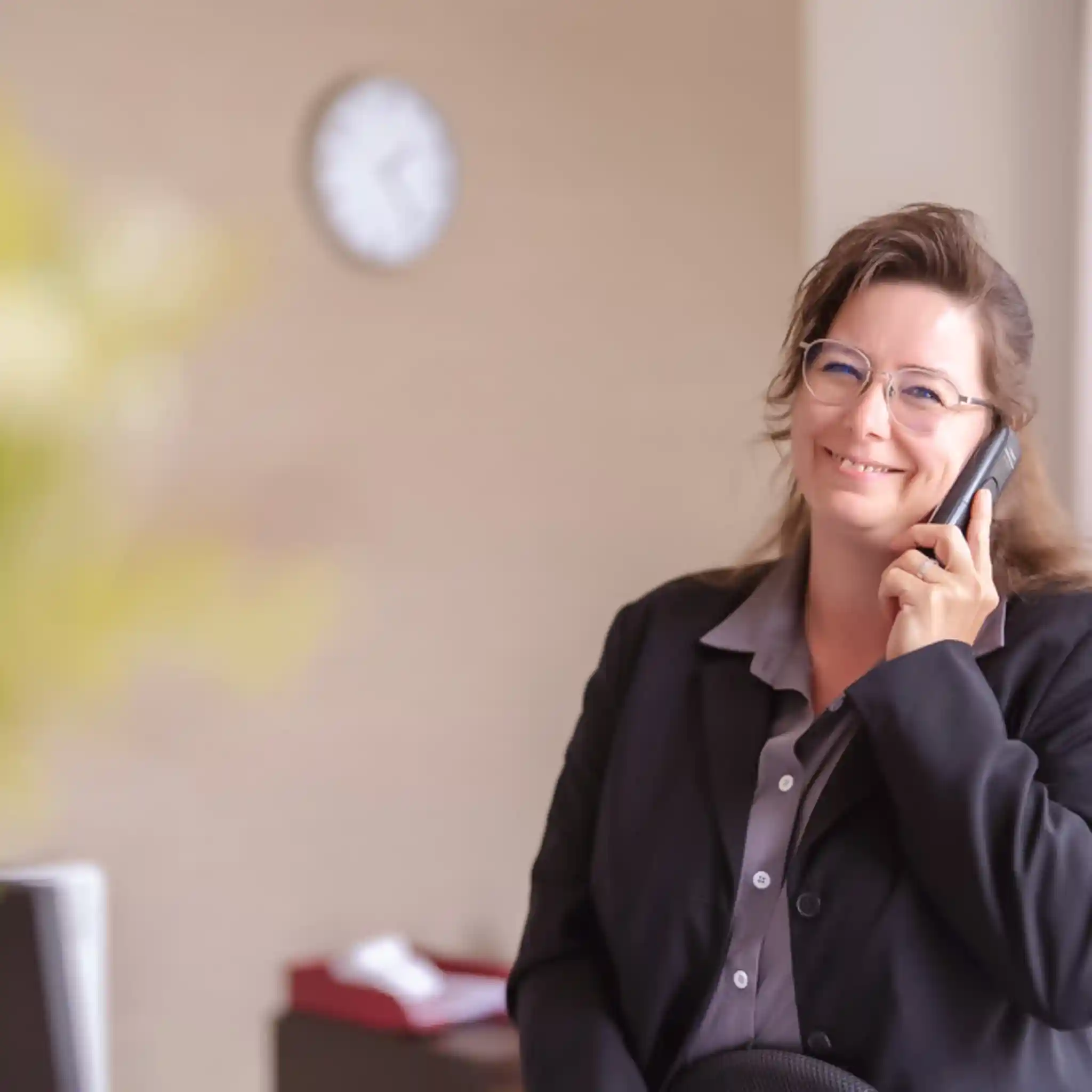 Eine Patientenmanagerin lacht in die Kamera, während sie sich ein Telefon ans Ohr hält.