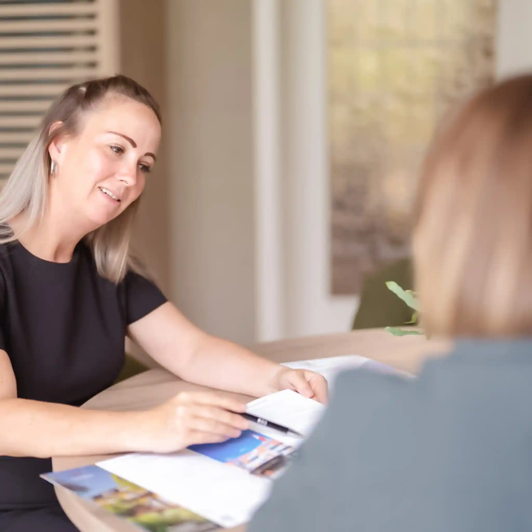 Eine Patientenmanagerin sitzt mit einer Patientin am Tisch und zeigt ihr die Informationsmaterialien.
