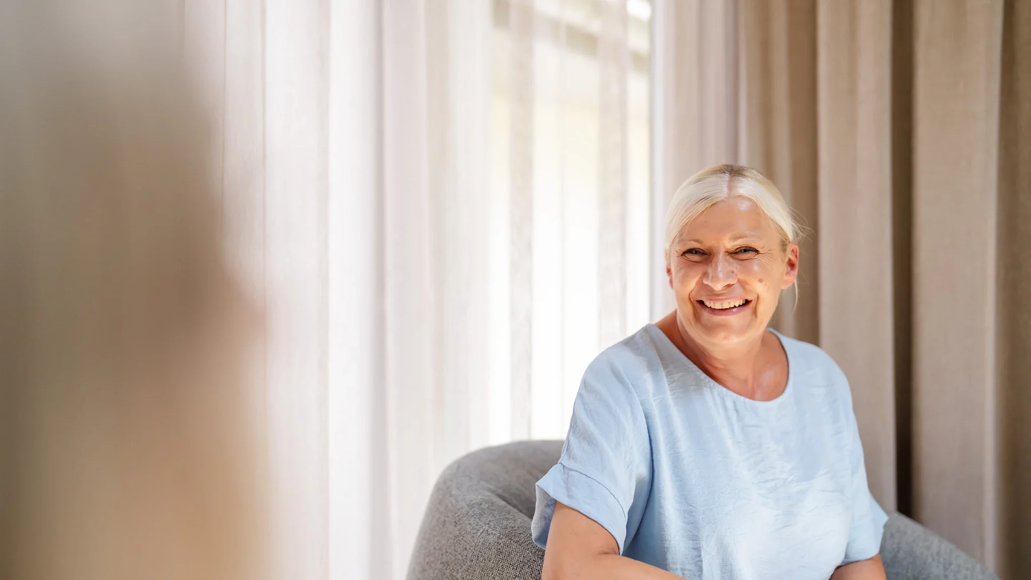 Eine Patientin lacht und strahlt ihre Ärztin an, die ihr gegenüber sitzt.