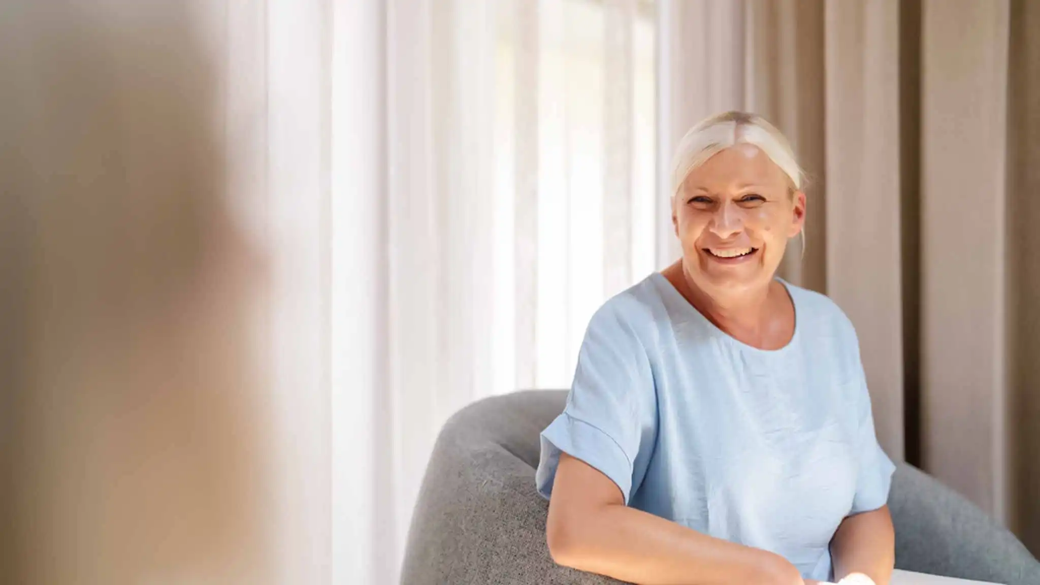 Eine Patientin lacht und strahlt ihre Ärztin an, die ihr gegenüber sitzt.