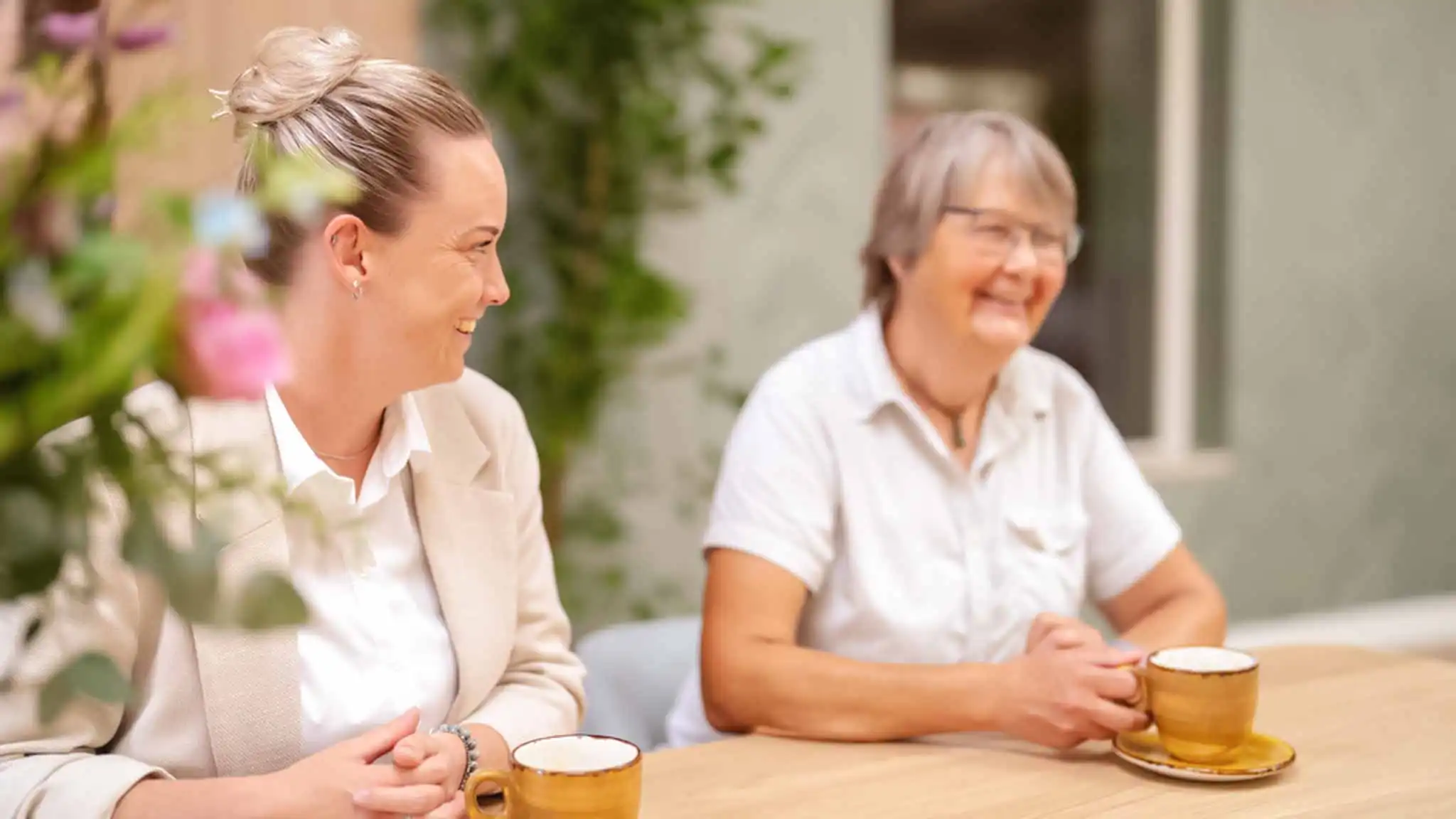 Zwei Mitarbeiterinnen trinken gemeinsam Kaffee und lachen.