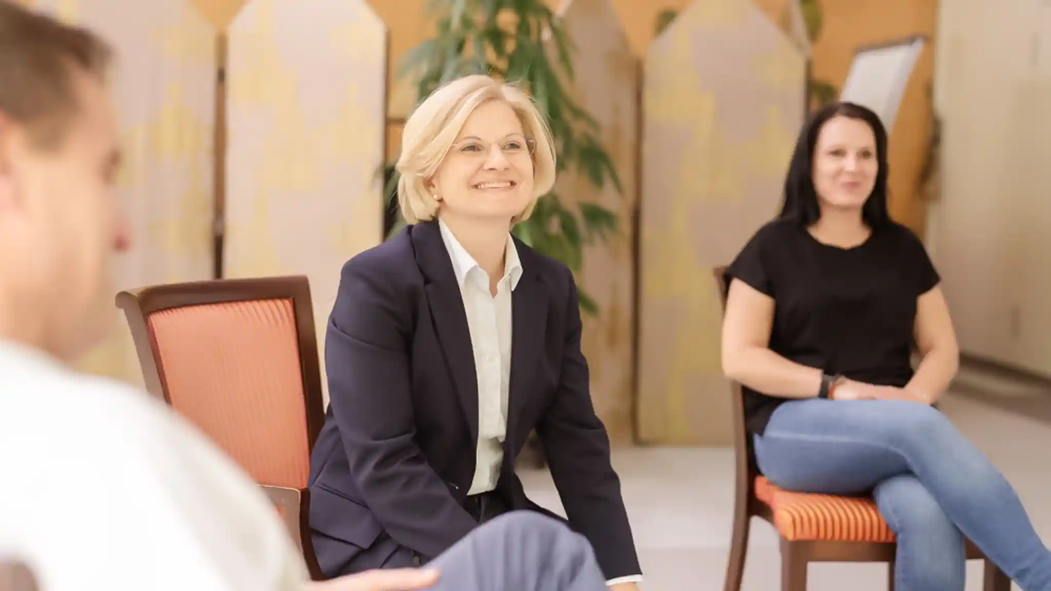 Eine Ärztin sitzt mit einigen Patienten in einem Stuhlkreis. Sie lacht fröhlich.