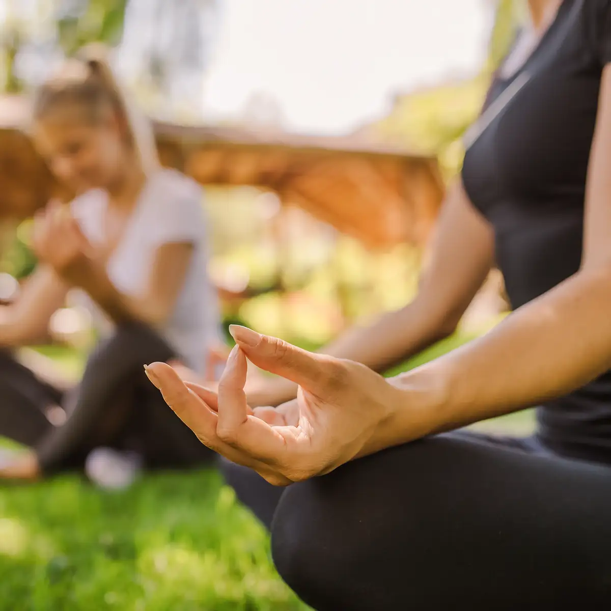 Eine Frau sitzt bei der Meditation im Schneidersitz. Sie hat Daumen und Zeigefinger aneinandergelegt.
