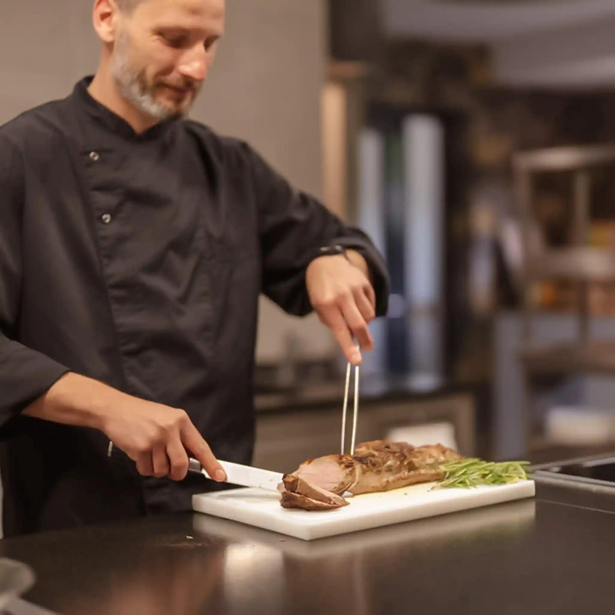 Ein Koch schneidet ein Stück Fleisch in Scheiben.