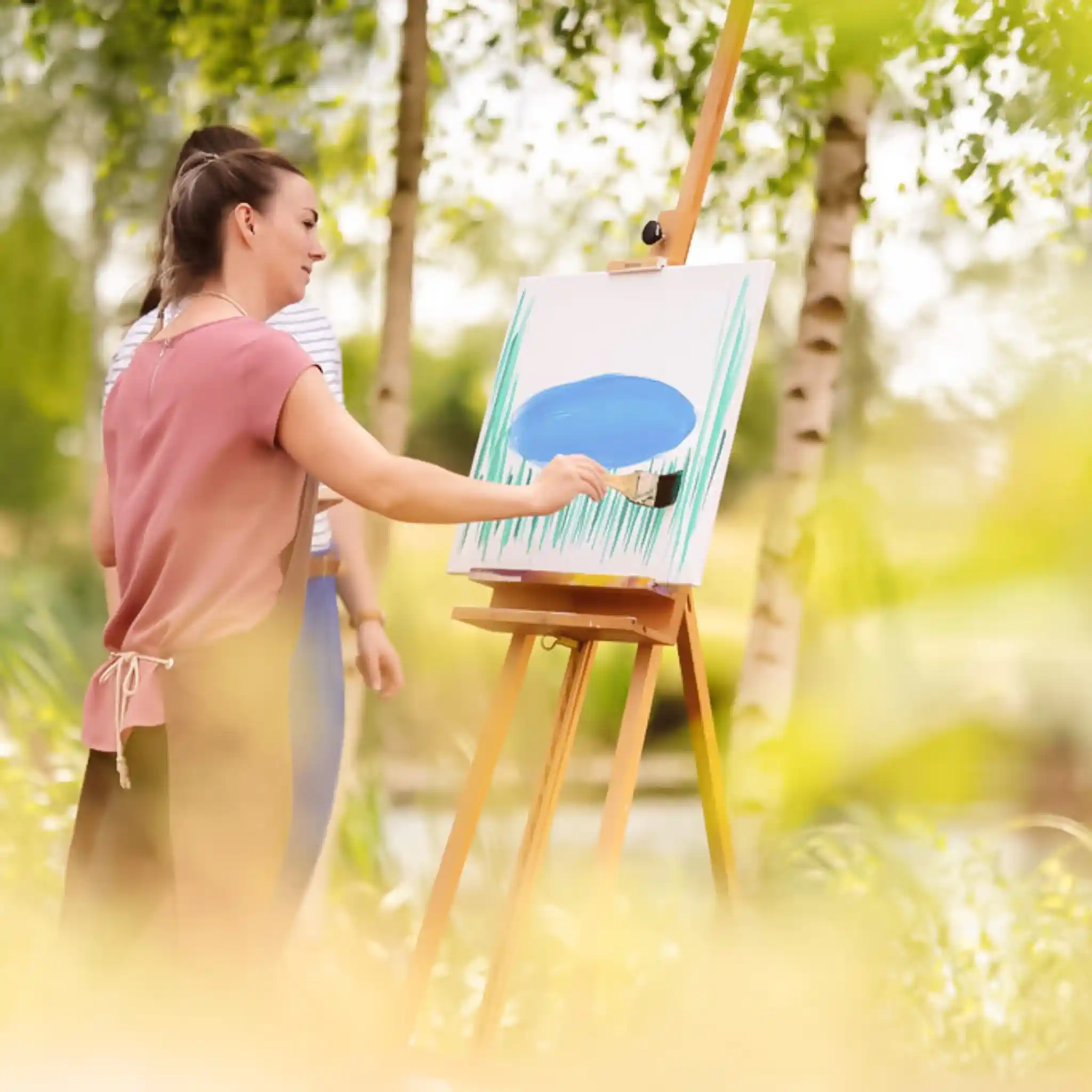 Eine Patientin malt in der Natur auf einer Leinwand.