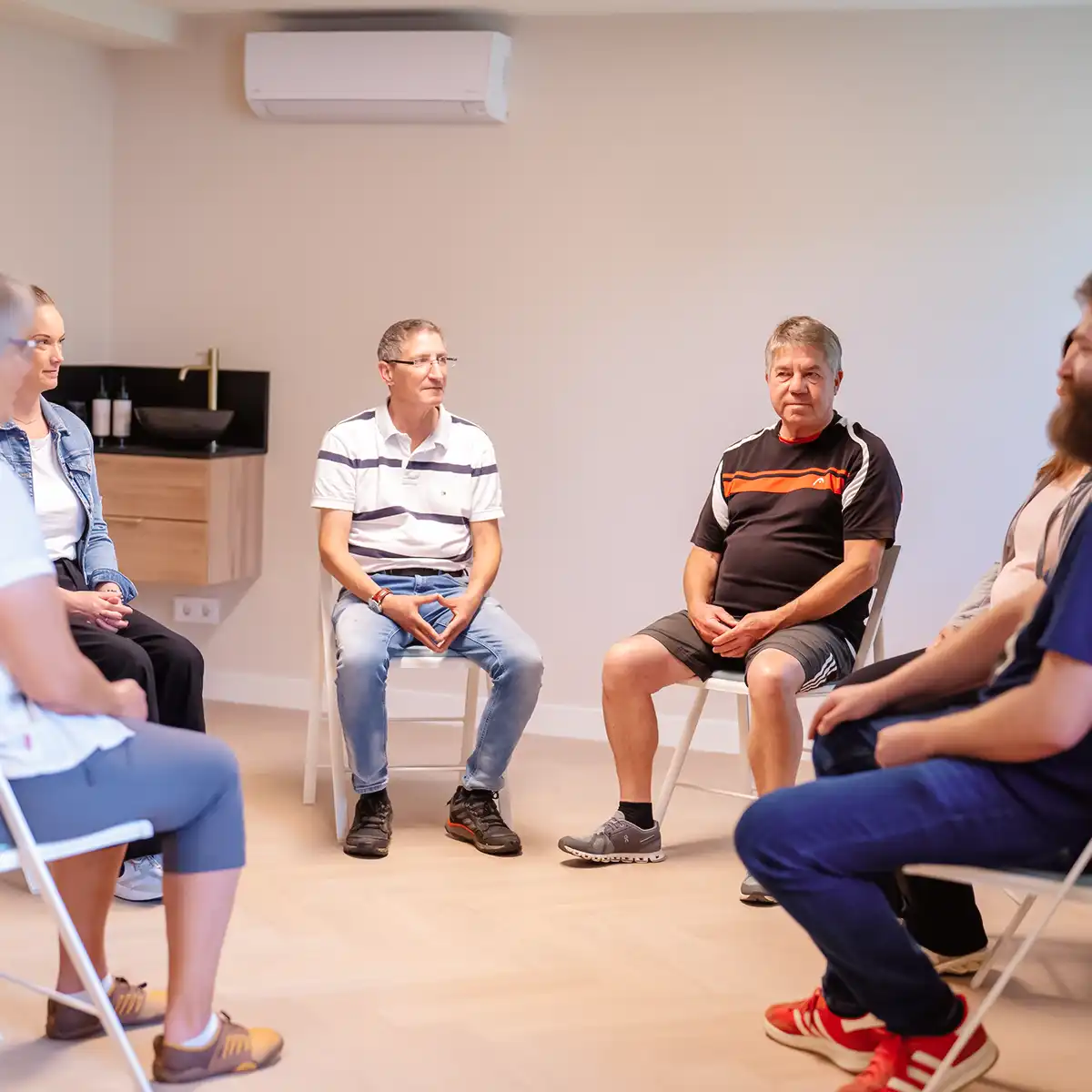 Sechs Patienten sitzen in einem Kreis und nehmen gemeinsam an einer Gruppentherapie teil.