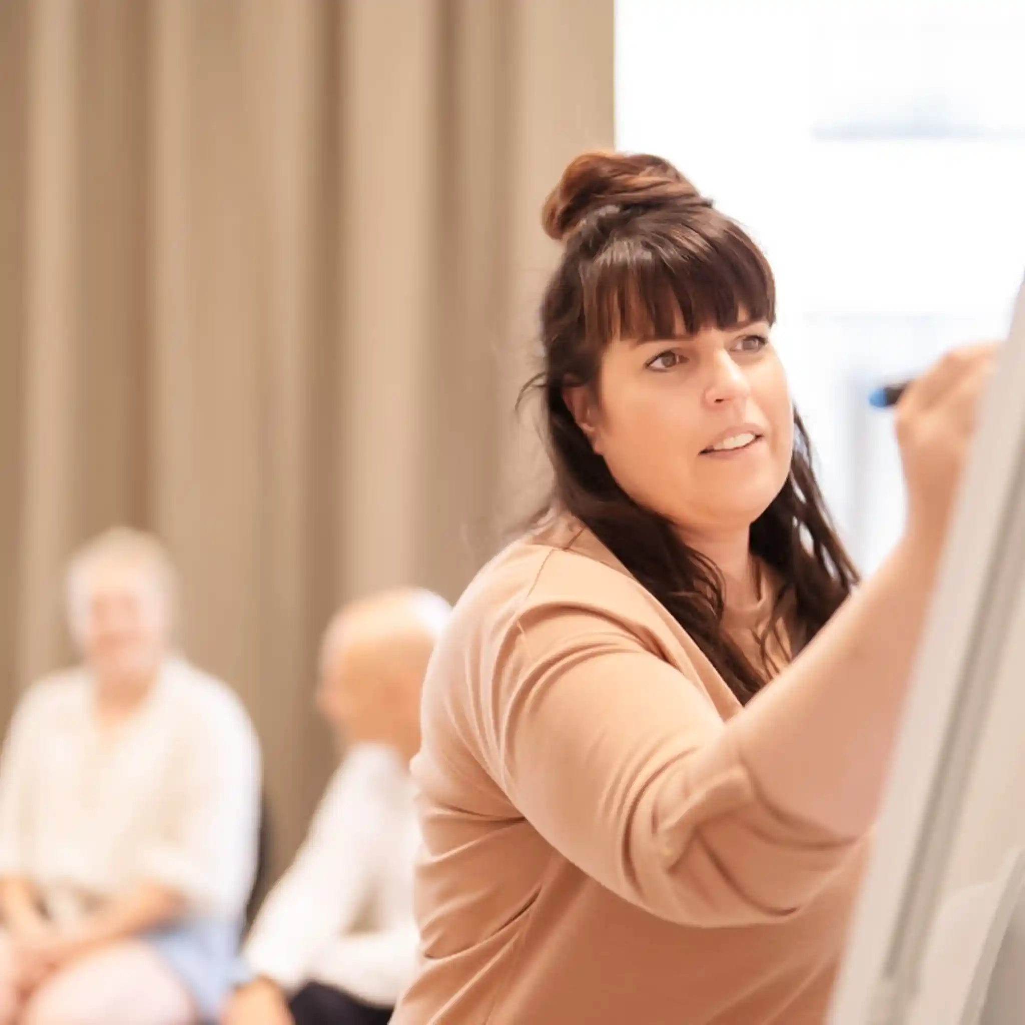 Eine Psychotherapeutin schreibt im Rahmen einer Gruppentherapie etwas auf ein Whiteboard.
