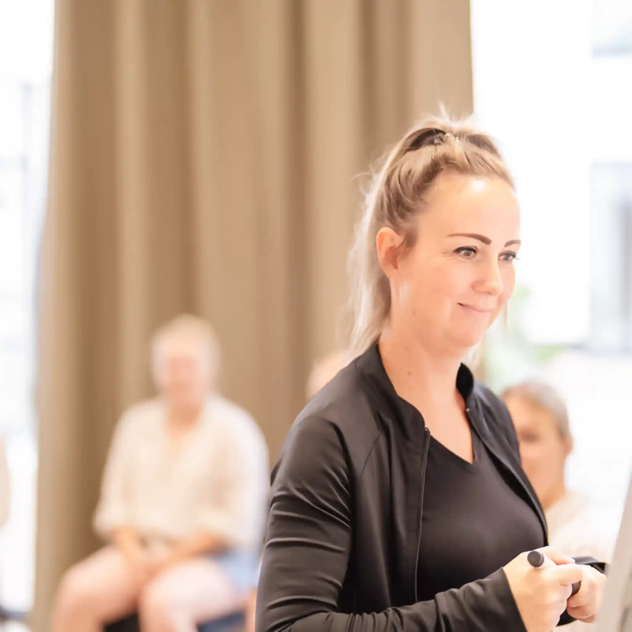 Eine Therapeutin öffnet ihren Stift, um etwas auf ein Whiteboard zu schreiben. Hinter ihr sitzen einige Personen.