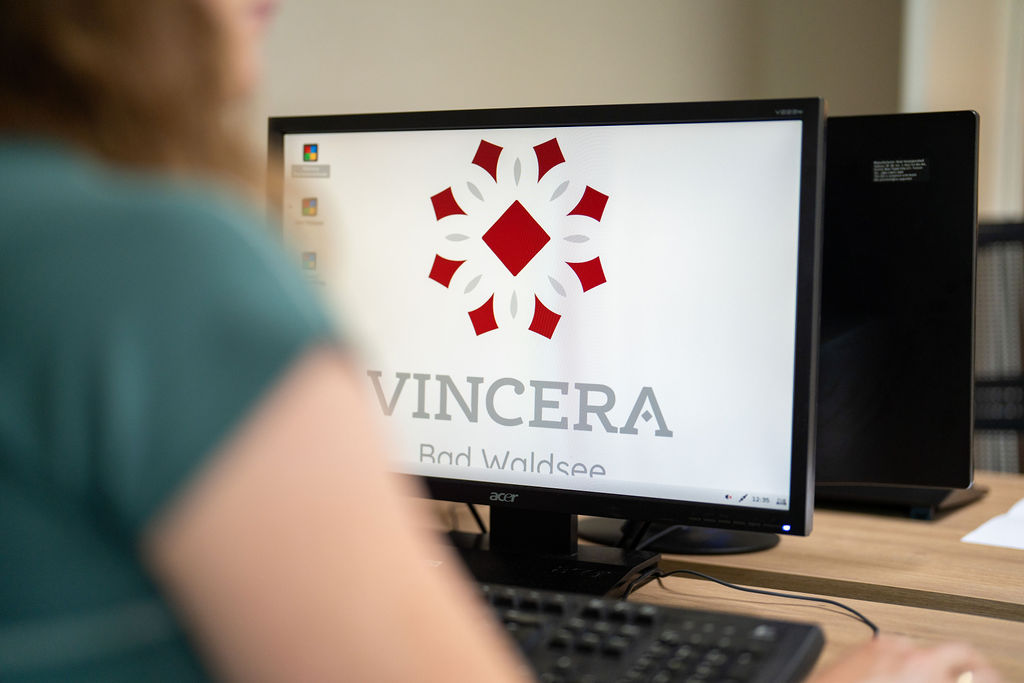 Eine Person sitzt an einem Schreibtisch vor einem Computerbildschirm, auf dem das Logo und der Schriftzug von VINCERA Bad Waldsee zu sehen sind.