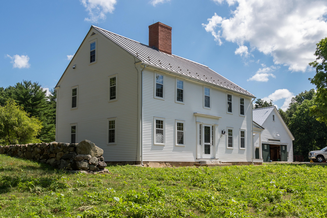 Restored historic white clapboard house with a red brick chimney and blue sky background.