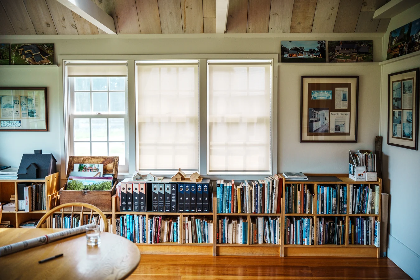 Architect’s studio with bookshelves filled with design books and binders, architectural models on display, and framed project features on the wall.
