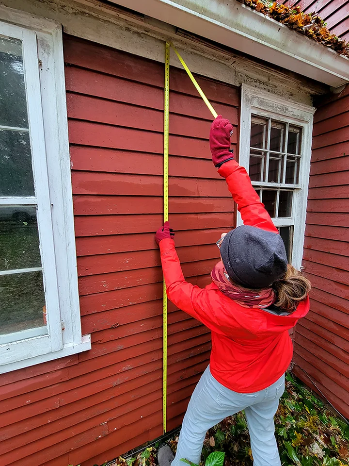 Architect measuring the exterior of a red historic house with a tape measure.