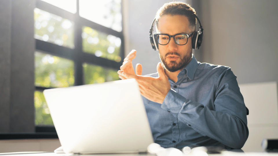 A man with glasses and headphones sits at a desk, focused on his laptop during AOTA's Complimentary Webinars.