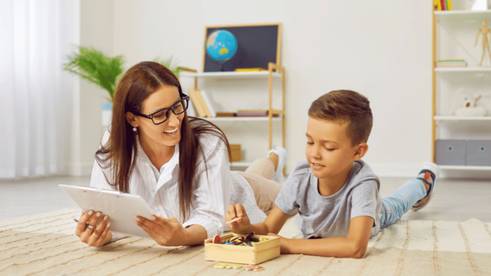 A woman and a boy are lying on the floor, engaged with a tablet, in a private practice speech-language pathology setting
