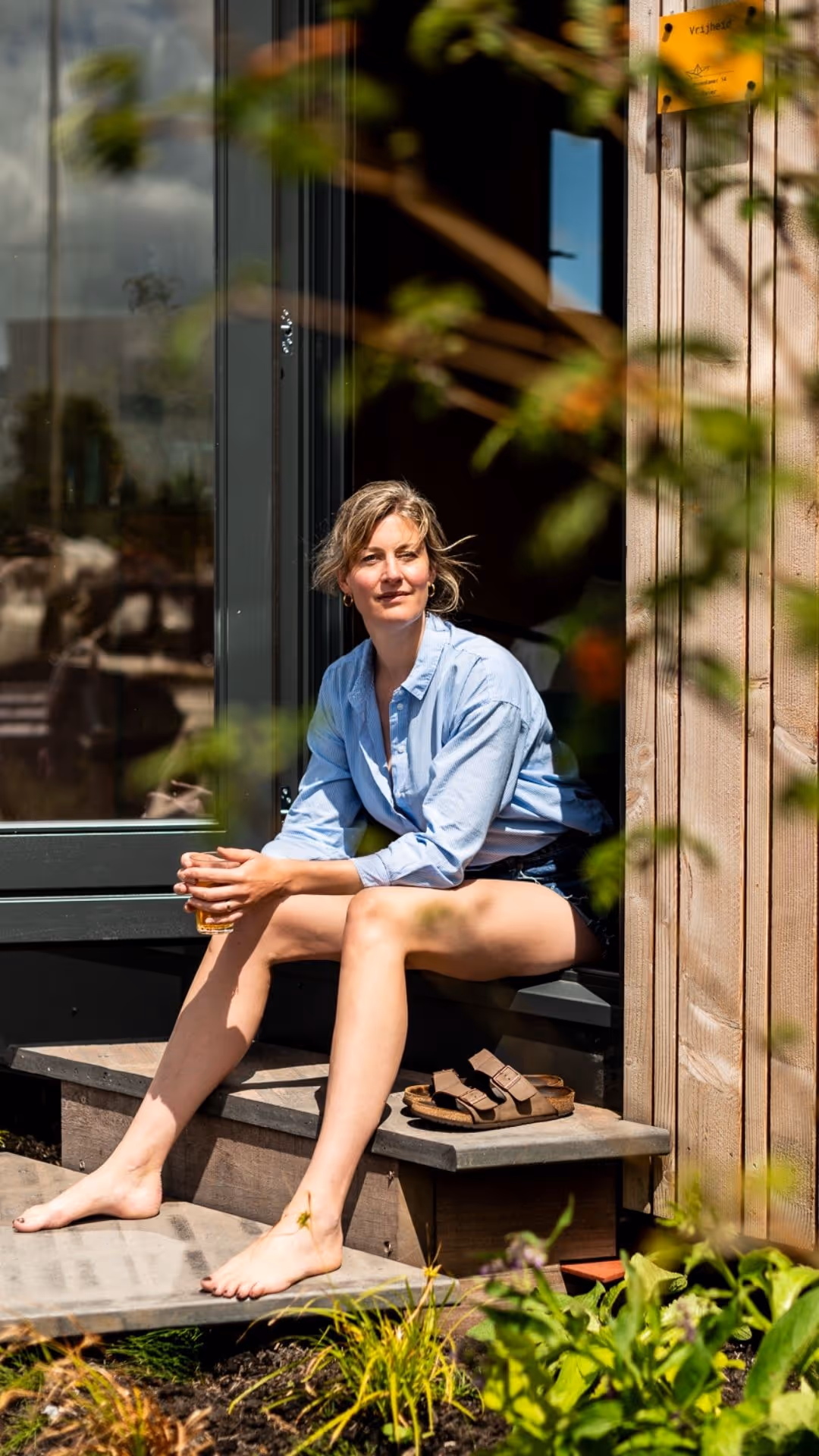 Een vrouw met een koffietje, in de zon, in de Kas