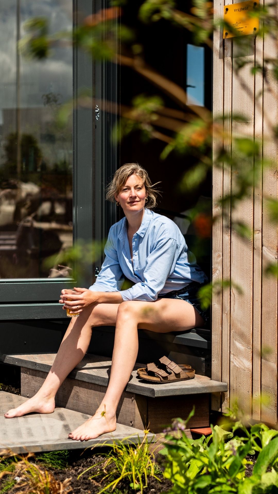 Een vrouw met een koffietje, in de zon, in de Kas