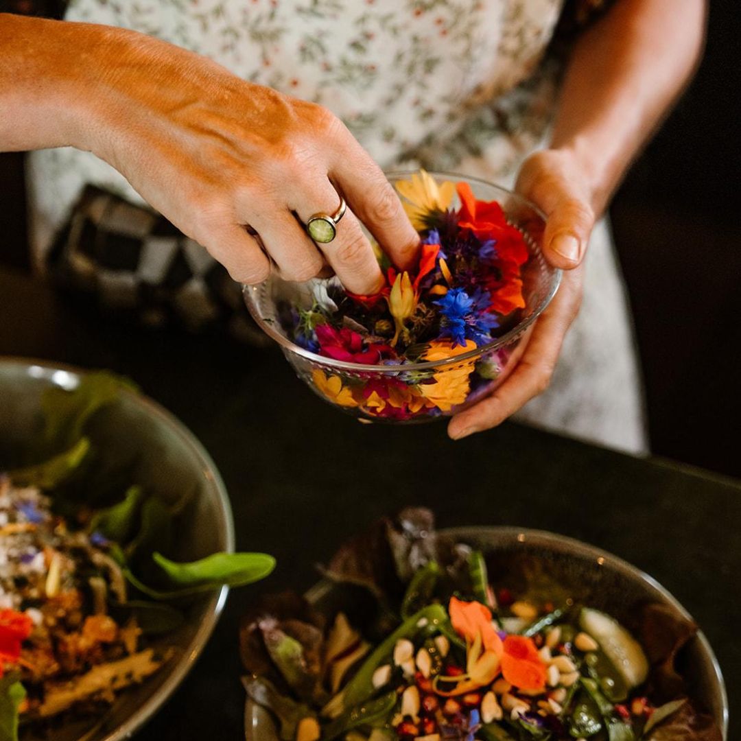 Handen die eetbare bloemen over een salade strooien