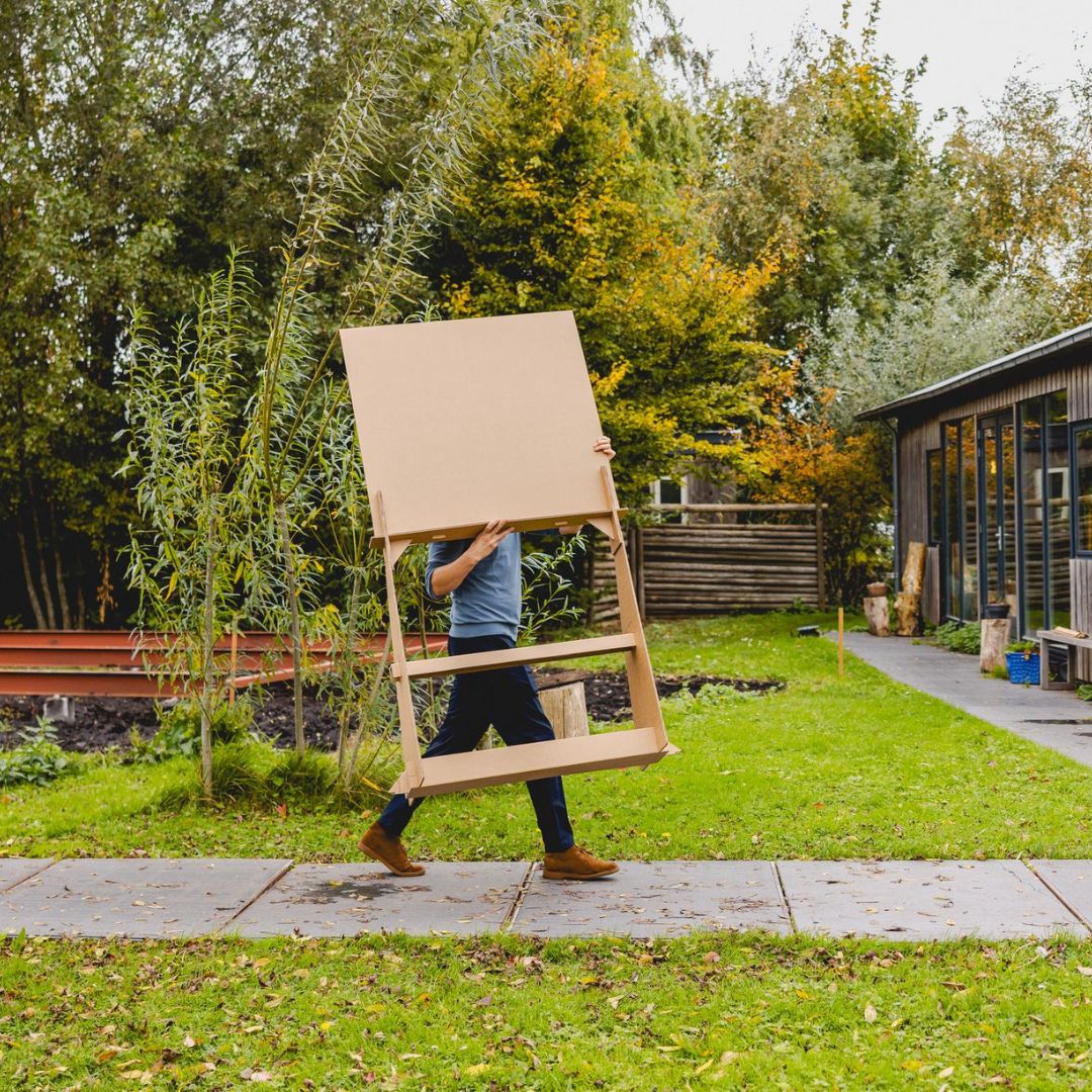 Man die een groot kartonnen bord door de tuin draagt