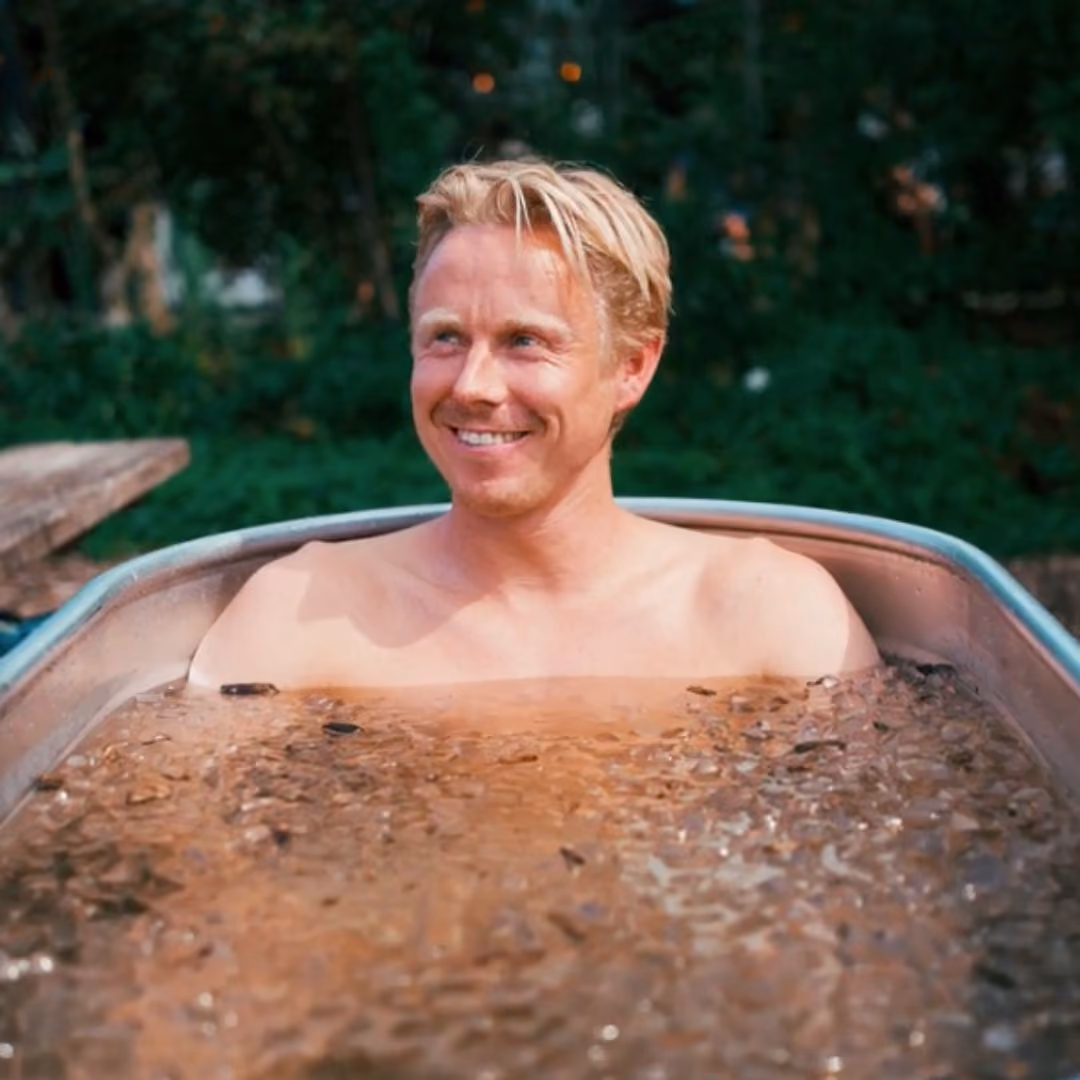 Man die glimlacht in een ijsbad in de tuin