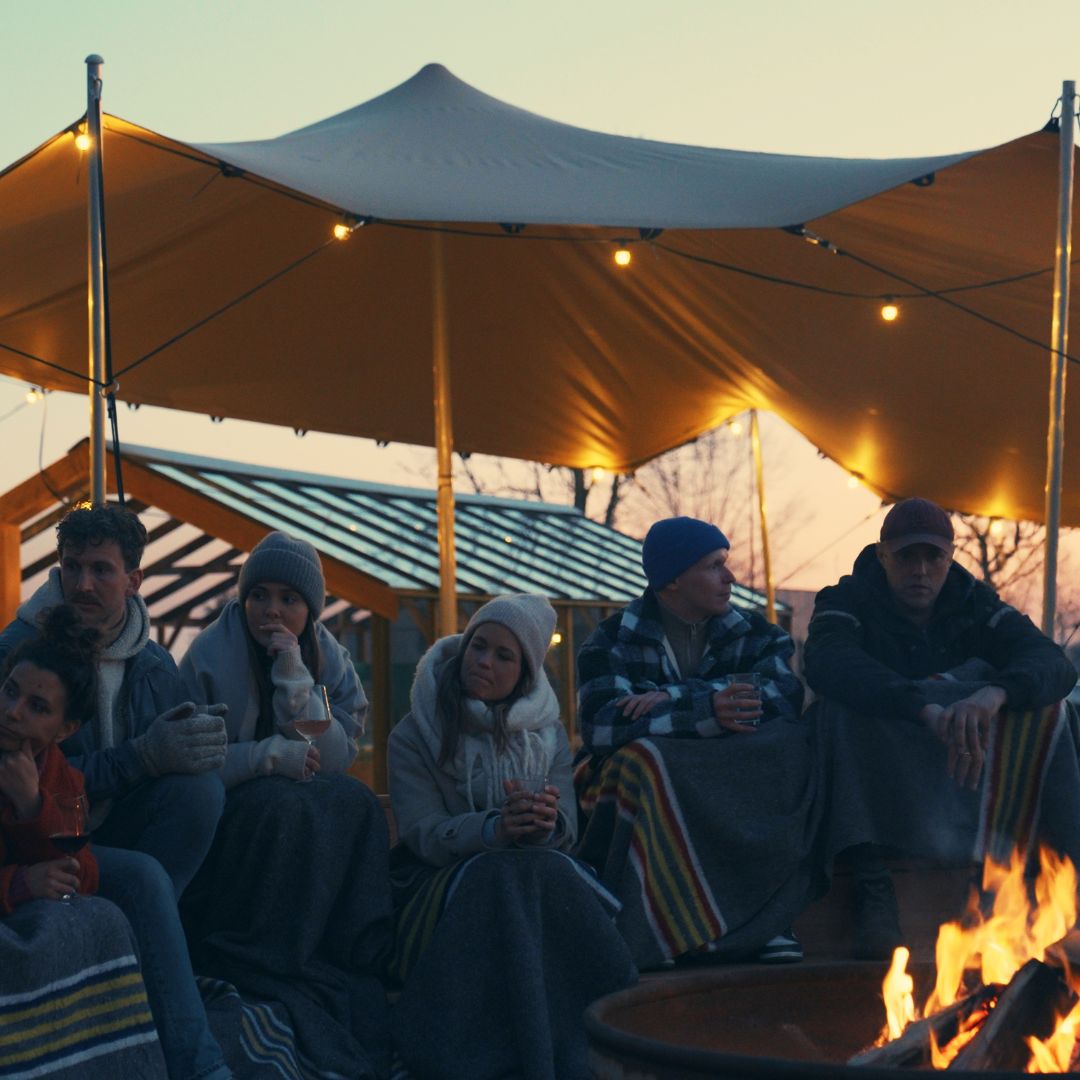 Groep bij het vuur onder een tent, gewikkeld in dekens met een drankje